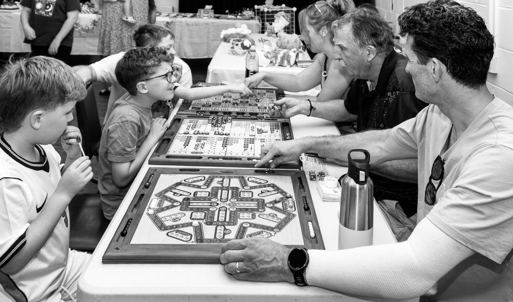 Families playing handcrafted wooden board games at a Norfolk Boards table